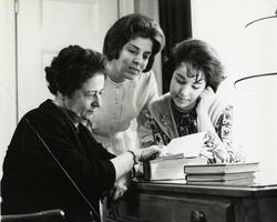 Two students and Professor of French Dr. Dora Bell examining books